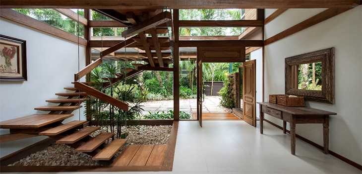 Hall de entrada de casa com jardim interno embaixo de uma escada de madeira