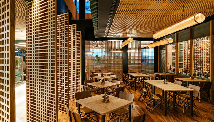 Foto da área interna do restaurante Adega Santiago SP, projetado por Bernardes Arquitetura. Há brises de madeira em toda a lateral do ambiente, conectando interior e exterior. 