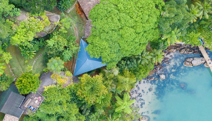 Foto aérea de um telhado em formato triangular e três quedas diferentes no meio de muita vegetação e água do mar 