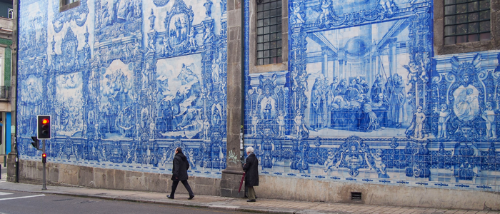 Pessoas passando em frente à grande prédio com fachada totalmente revestida com azulejo português, que mostra diferentes cenas do cotidiano
