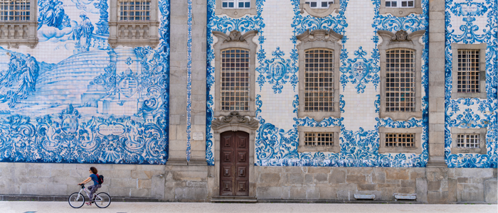 Homem andando de bicicleta em frente à grande prédio com azulejo português na fachada